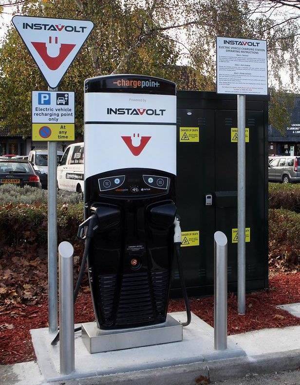Instavolt electric vehicle charging unit installed in a car park, with charging cables and parked cars in the background