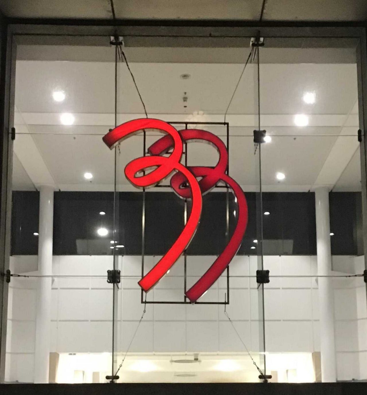 Red sculptural logo displayed inside a modern building with glass walls and ceiling lights